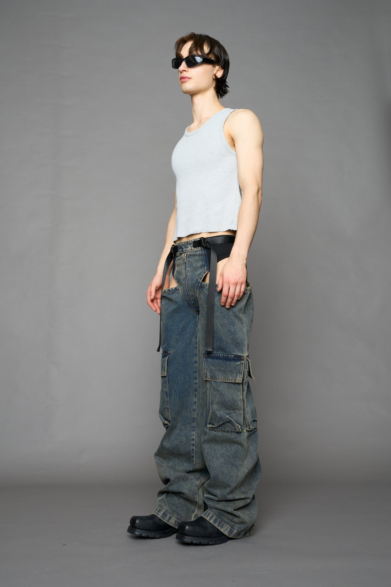 model wearing blue mud washed denim trousers with cut out design and 3D pockets