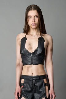 Model in bold black vegan leather statement halter top with provocative cup design and front zipper, paired with matching pants – futuristic streetwear look