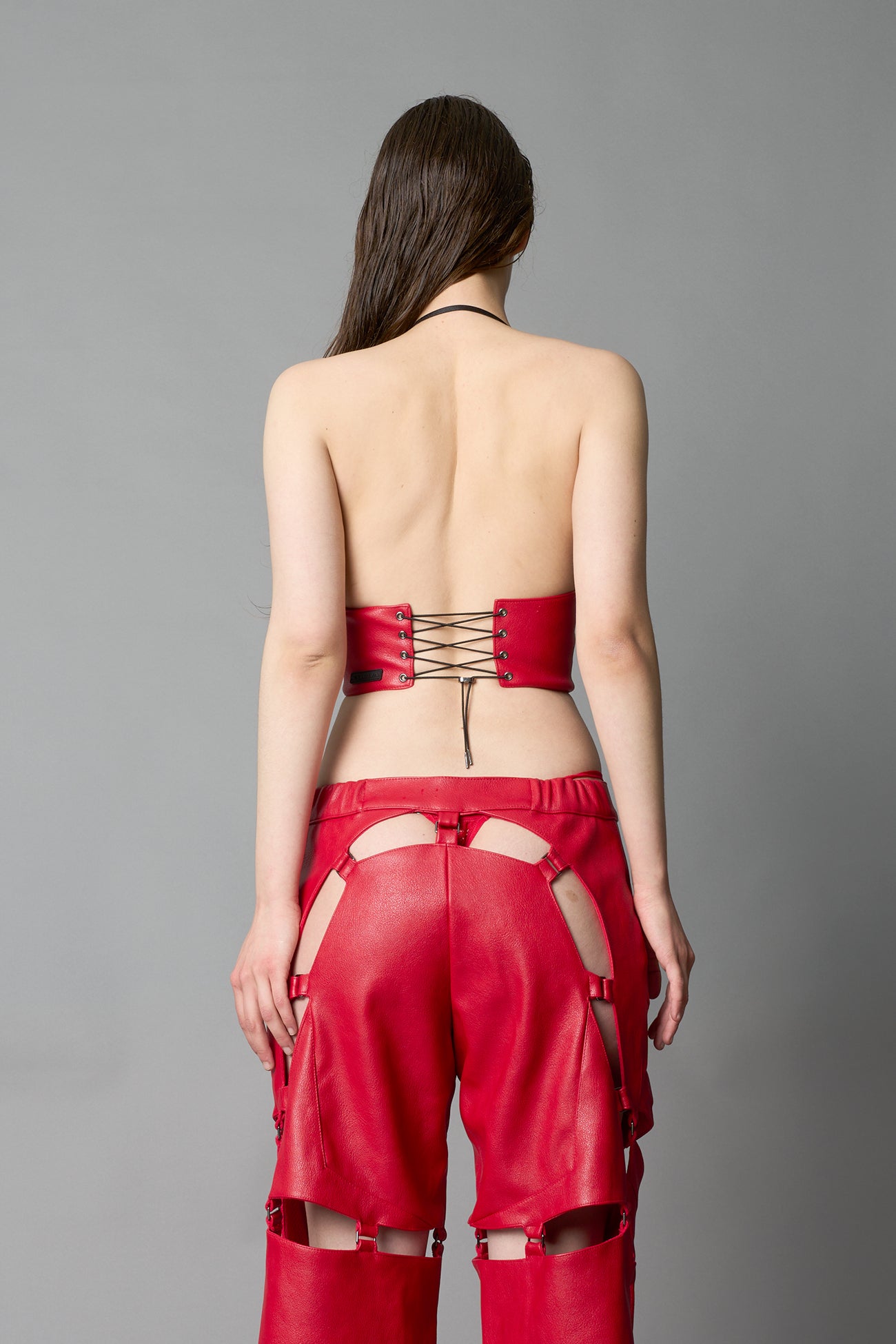 Model in bold red vegan leather statement halter top with provocative cup design and front zipper, paired with matching pants – futuristic streetwear look