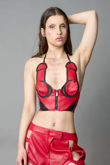 Model in bold red vegan leather statement halter top with provocative cup design and front zipper, paired with matching pants – futuristic streetwear look