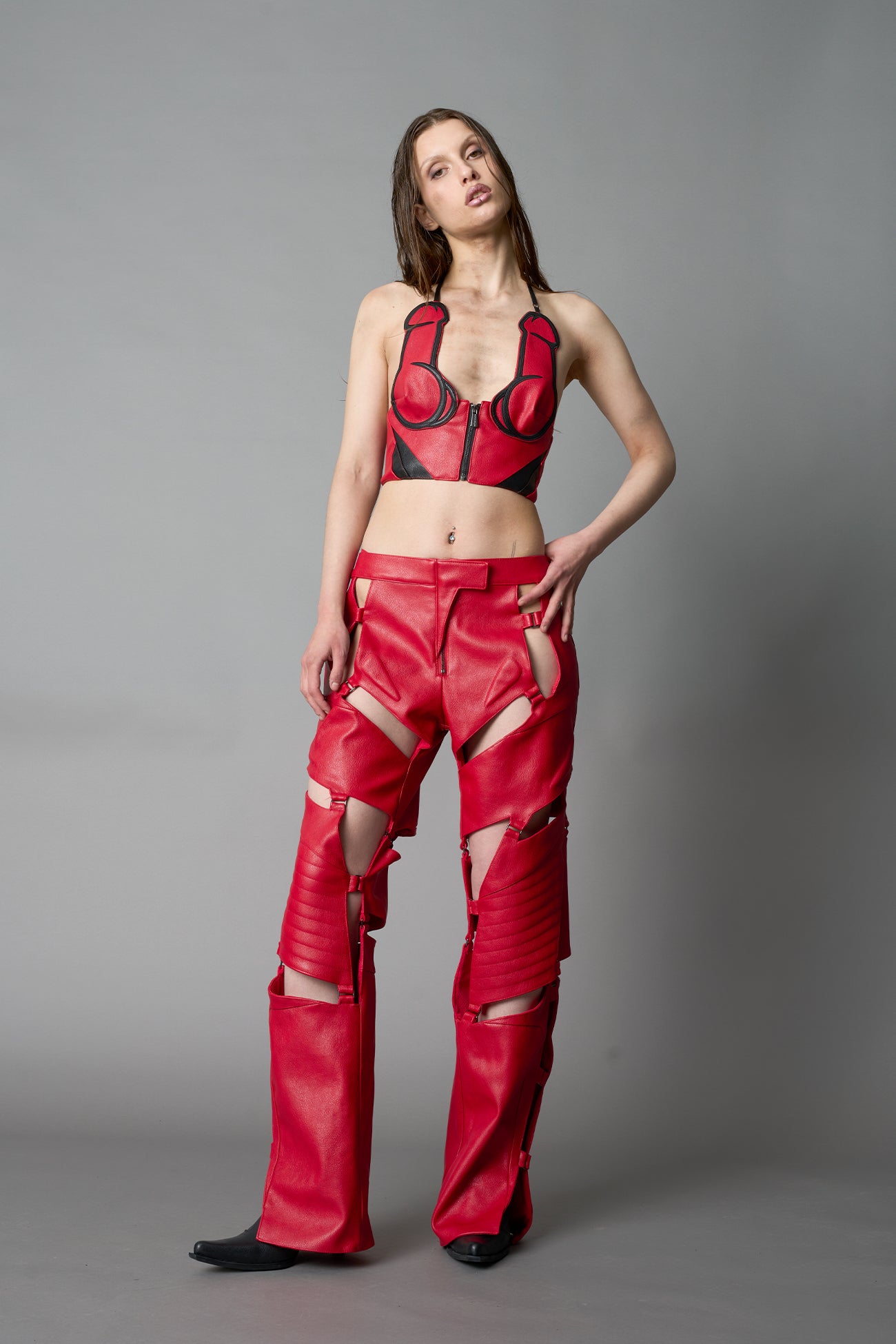 Model in bold red vegan leather statement halter top with provocative cup design and front zipper, paired with matching pants – futuristic streetwear look