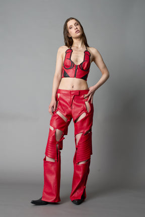 Model in bold red vegan leather statement halter top with provocative cup design and front zipper, paired with matching pants – futuristic streetwear look