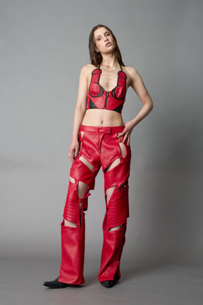 Model in bold red vegan leather statement halter top with provocative cup design and front zipper, paired with matching pants – futuristic streetwear look