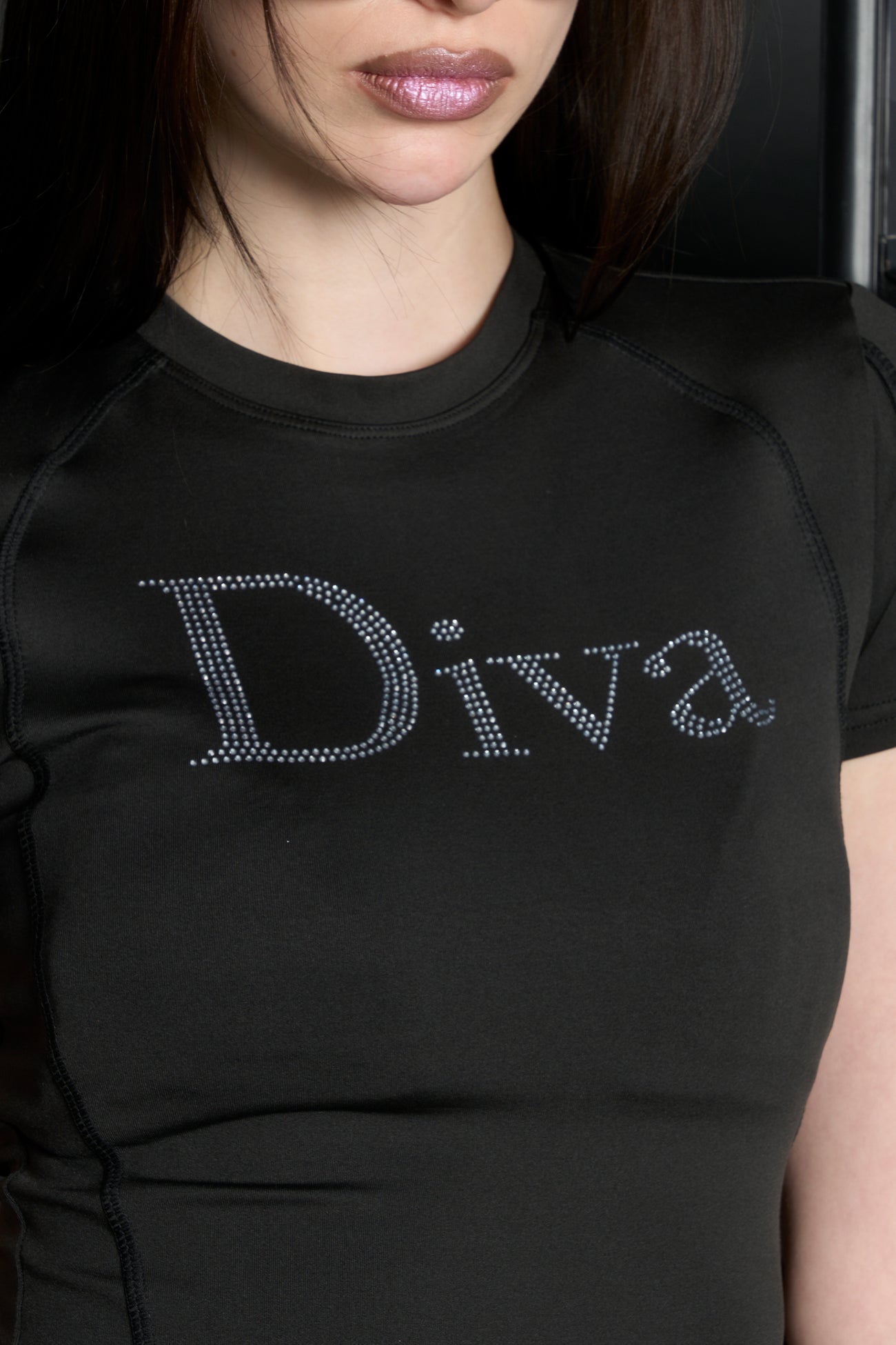 Model wears a black short-sleeved stretch lycra t-shirt with racing-style lines , black coverstitch seams, and a rhinestoned slogan.