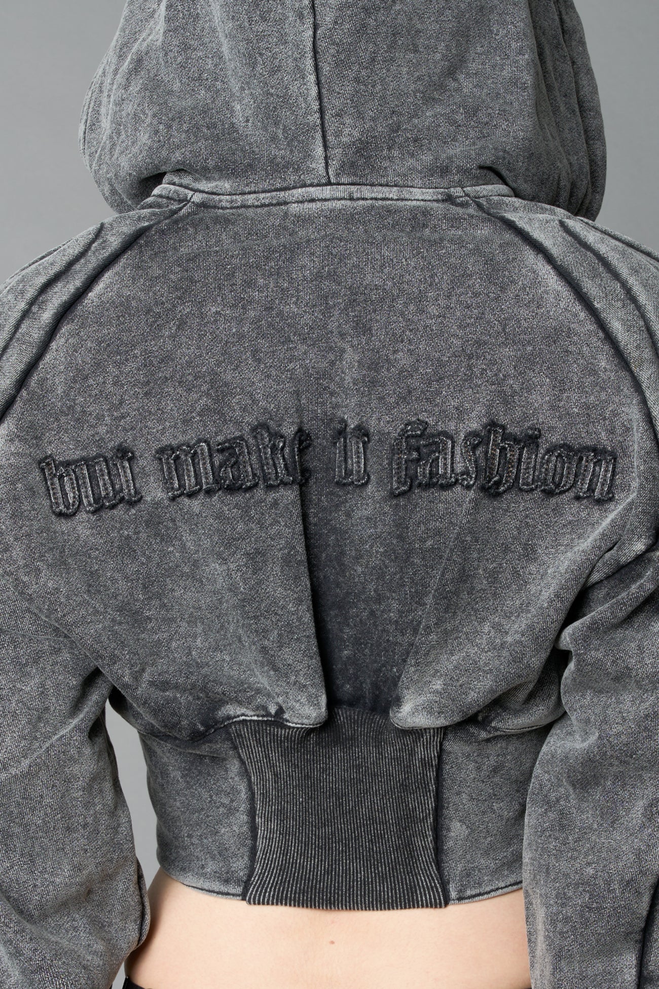 model in a washed-black cropped hoodie featuring structured corset-style paneling  embroidered across the chest in tonal black