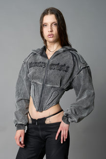 model in a washed-black cropped hoodie featuring structured corset-style paneling  embroidered across the chest in tonal black