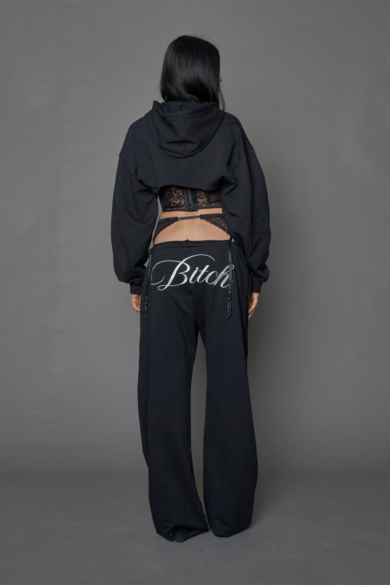 model wearing a black low waist jogger with a lace suspender belt and statement embroidery 