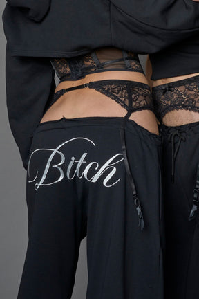 detail of a black low waist jogger with a lace suspender belt and statement embroidery 