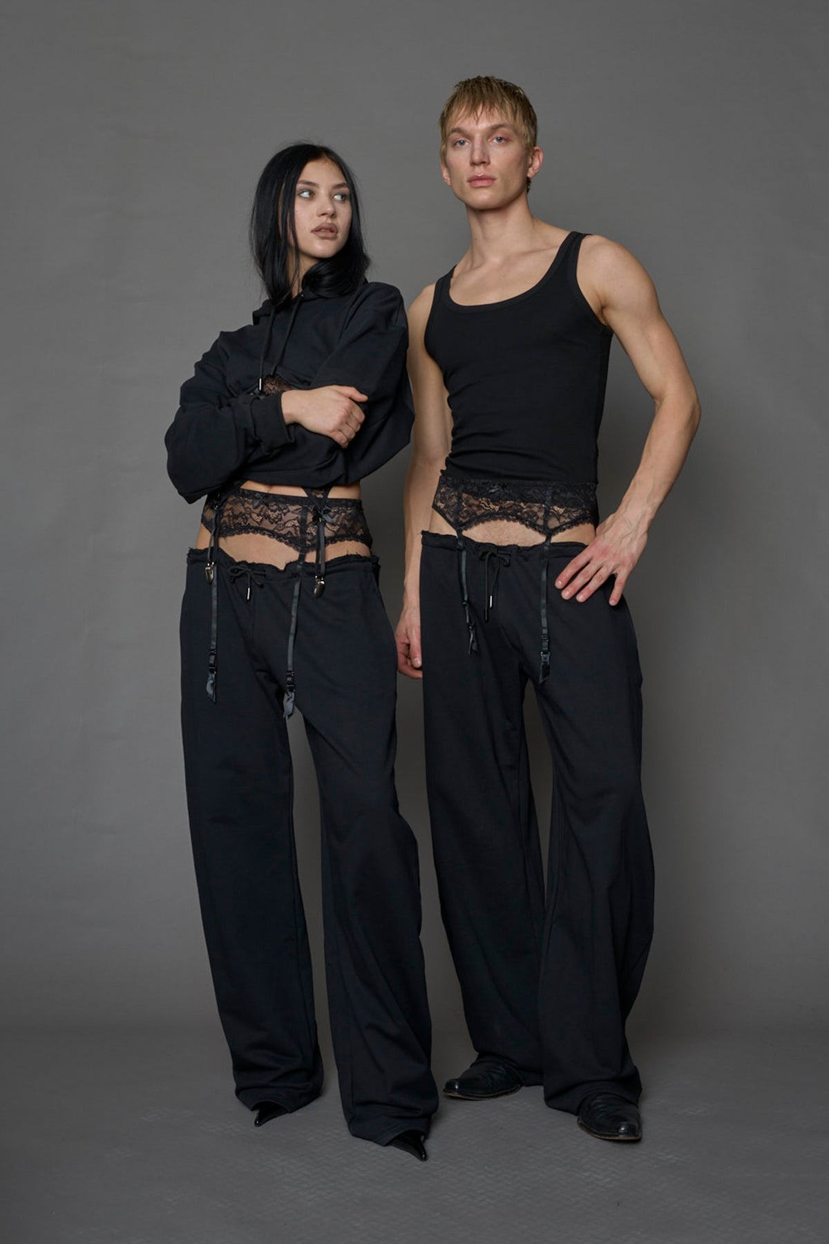 male and female model wearing a black low waist jogger with a lace suspender belt 