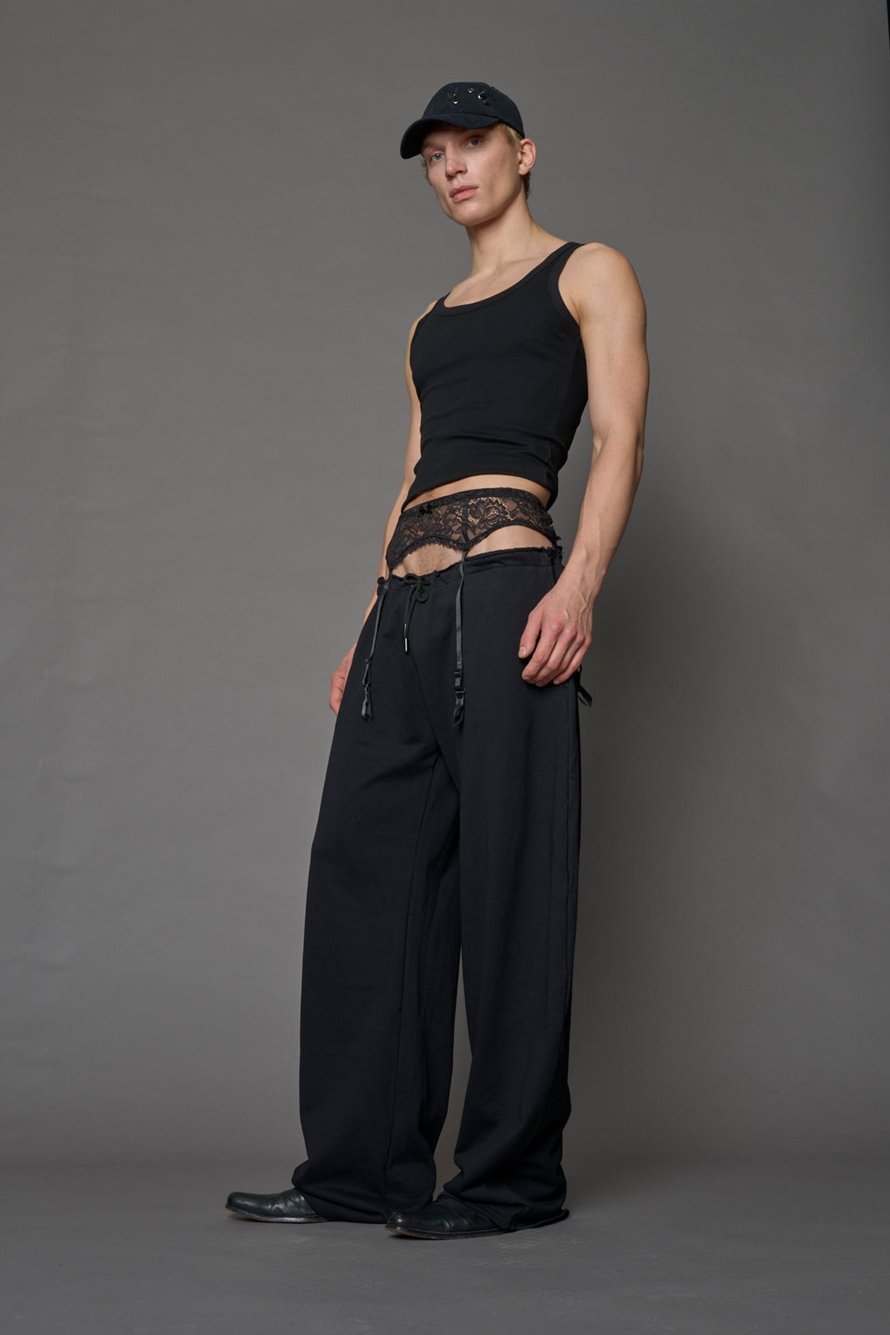 male model wearing a black low waist jogger with a lace suspender belt 