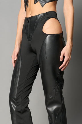 Black cut-out flare pants with graphic details, vegan leather panels, and low-rise waist – edgy motocross-inspired trousers for men’s streetwear or festival looks.