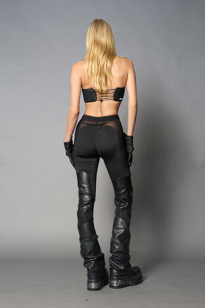 Model wearing high-waisted black vegan leather pants with mesh cutouts, moto-inspired paneling, and flared stacked legs – edgy streetwear trousers styled with chunky platform boots