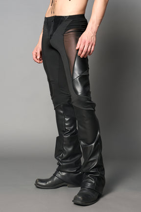 Model wearing high-waisted black vegan leather pants with mesh cutouts, moto-inspired paneling, and flared stacked legs – edgy streetwear trousers styled with chunky platform boots