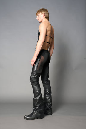 Model wearing high-waisted black vegan leather pants with mesh cutouts, moto-inspired paneling, and flared stacked legs – edgy streetwear trousers styled with chunky platform boots