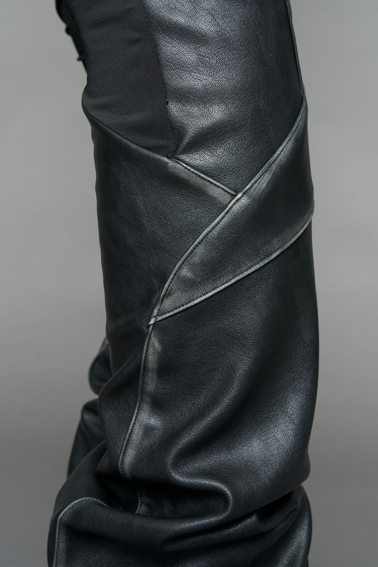 Model wearing high-waisted black washed vegan leather pants with mesh cutouts, moto-inspired paneling, and flared stacked legs – edgy streetwear trousers styled with chunky platform boots