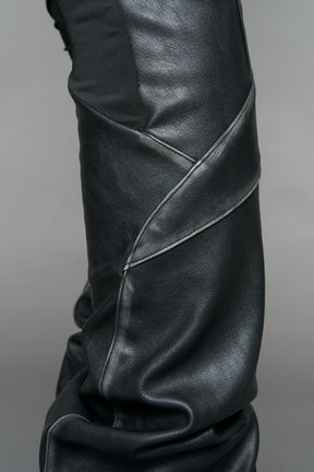 Model wearing high-waisted black washed vegan leather pants with mesh cutouts, moto-inspired paneling, and flared stacked legs – edgy streetwear trousers styled with chunky platform boots