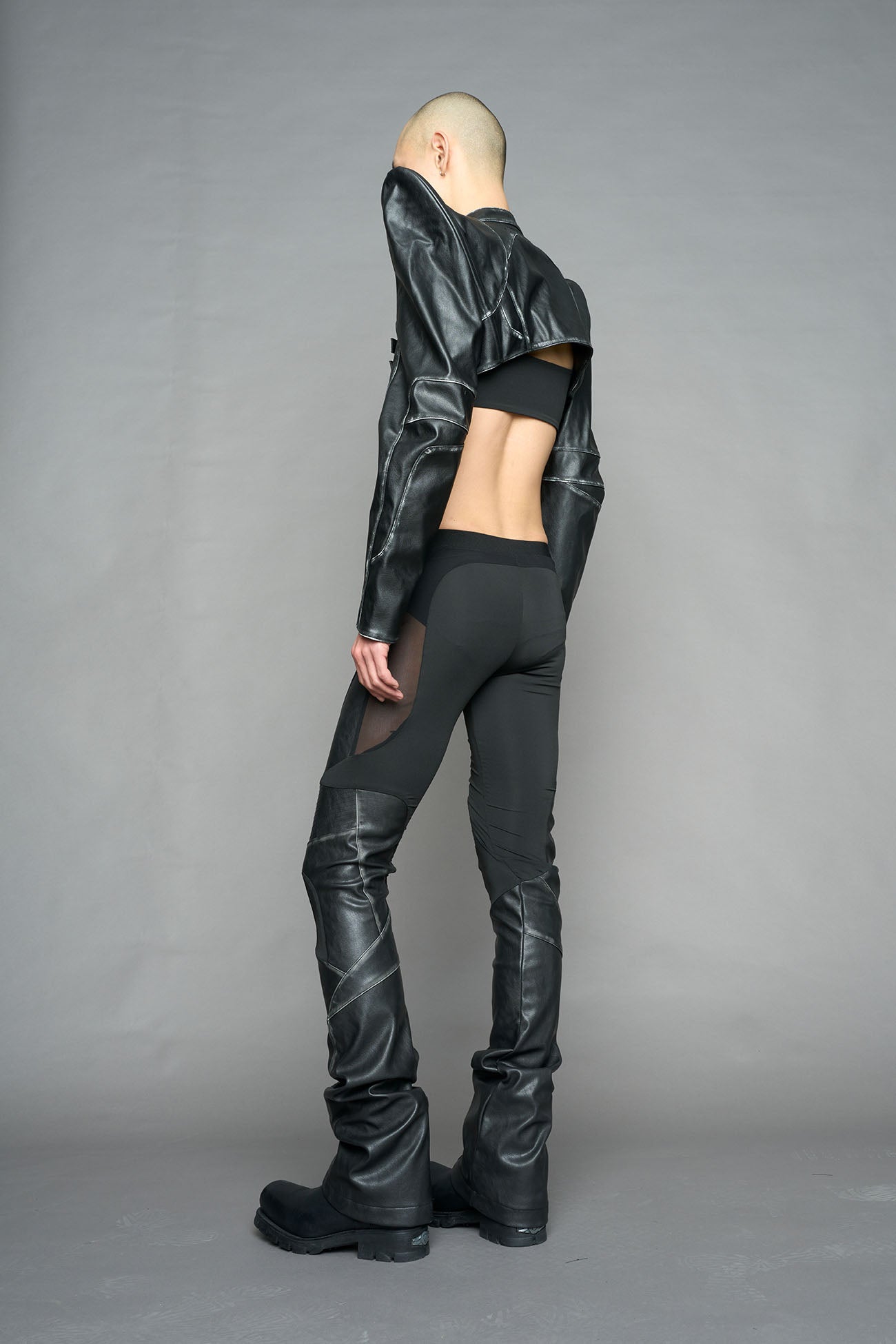 Model wearing high-waisted black washed vegan leather pants with mesh cutouts, moto-inspired paneling, and flared stacked legs – edgy streetwear trousers styled with chunky platform boots