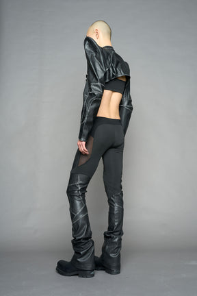 Model wearing high-waisted black washed vegan leather pants with mesh cutouts, moto-inspired paneling, and flared stacked legs – edgy streetwear trousers styled with chunky platform boots