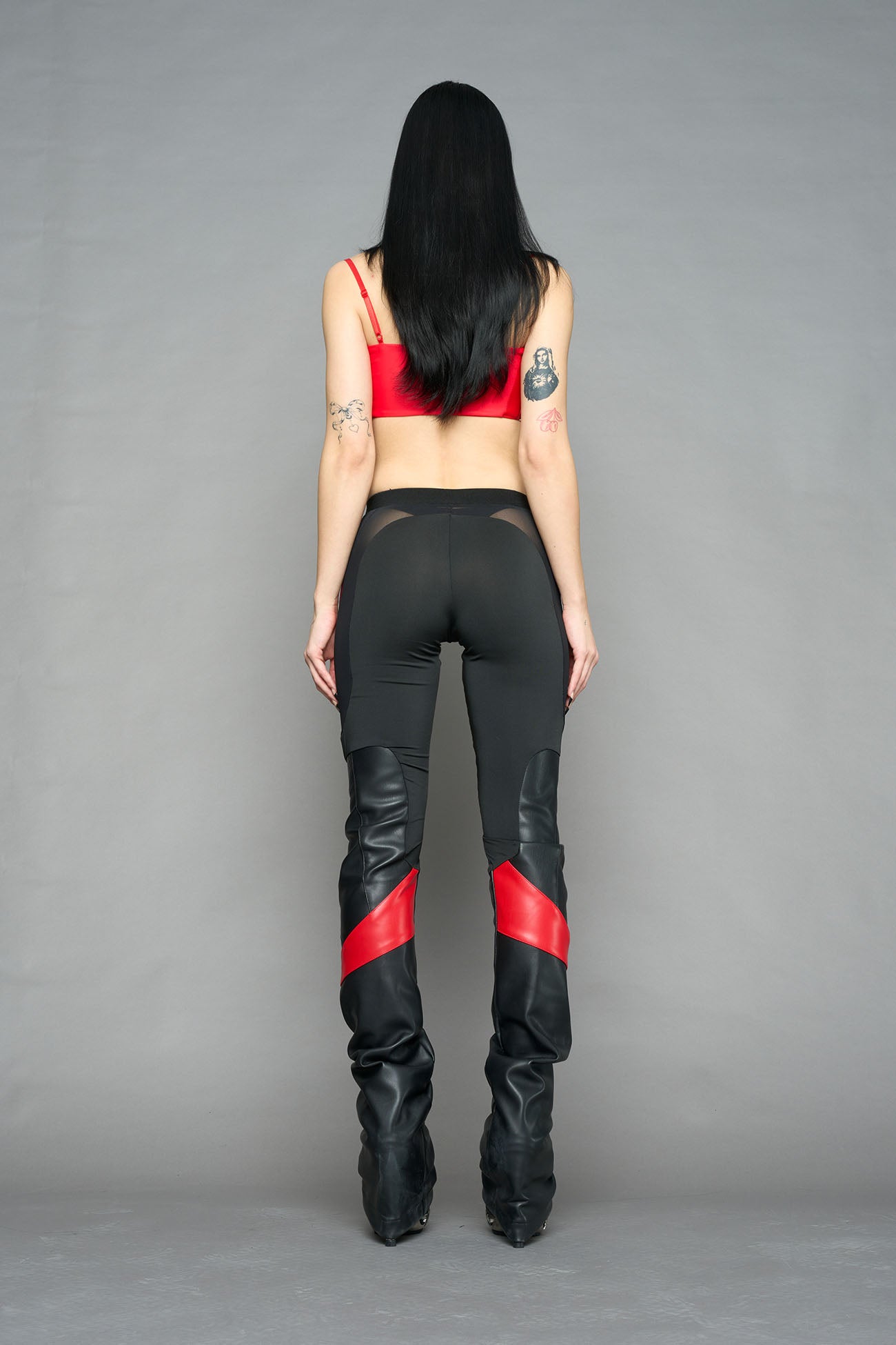 Model wearing high-waisted black red vegan leather pants with mesh cutouts, moto-inspired paneling, and flared stacked legs – edgy streetwear trousers styled with chunky platform boots