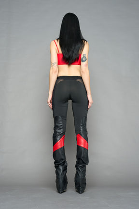 Model wearing high-waisted black red vegan leather pants with mesh cutouts, moto-inspired paneling, and flared stacked legs – edgy streetwear trousers styled with chunky platform boots
