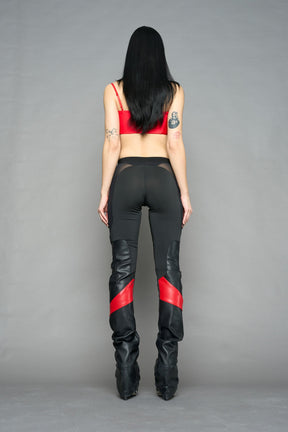 Model wearing high-waisted black red vegan leather pants with mesh cutouts, moto-inspired paneling, and flared stacked legs – edgy streetwear trousers styled with chunky platform boots