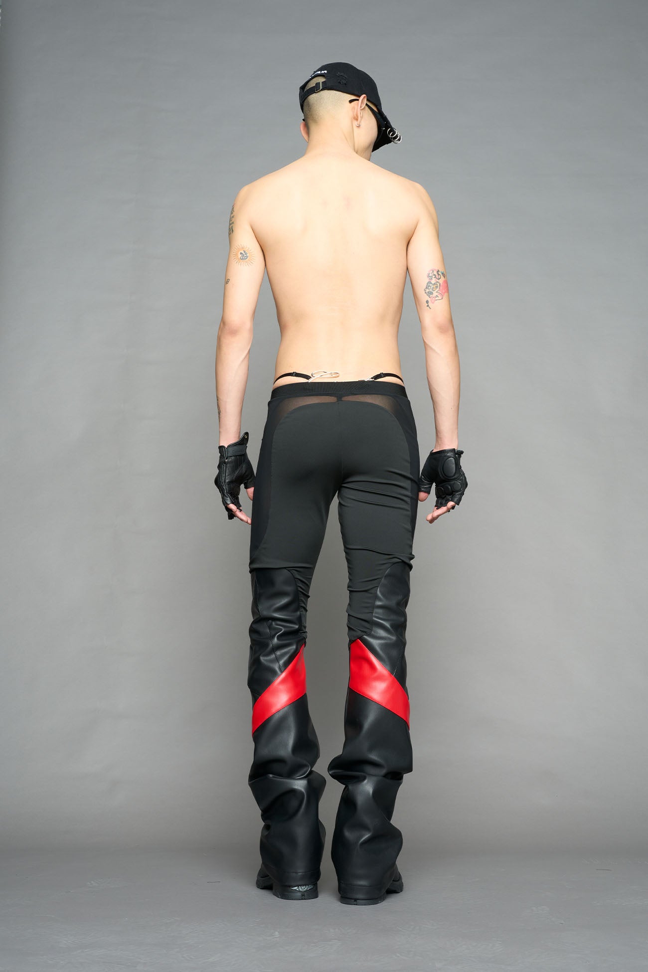 Model wearing high-waisted black red vegan leather pants with mesh cutouts, moto-inspired paneling, and flared stacked legs – edgy streetwear trousers styled with chunky platform boots