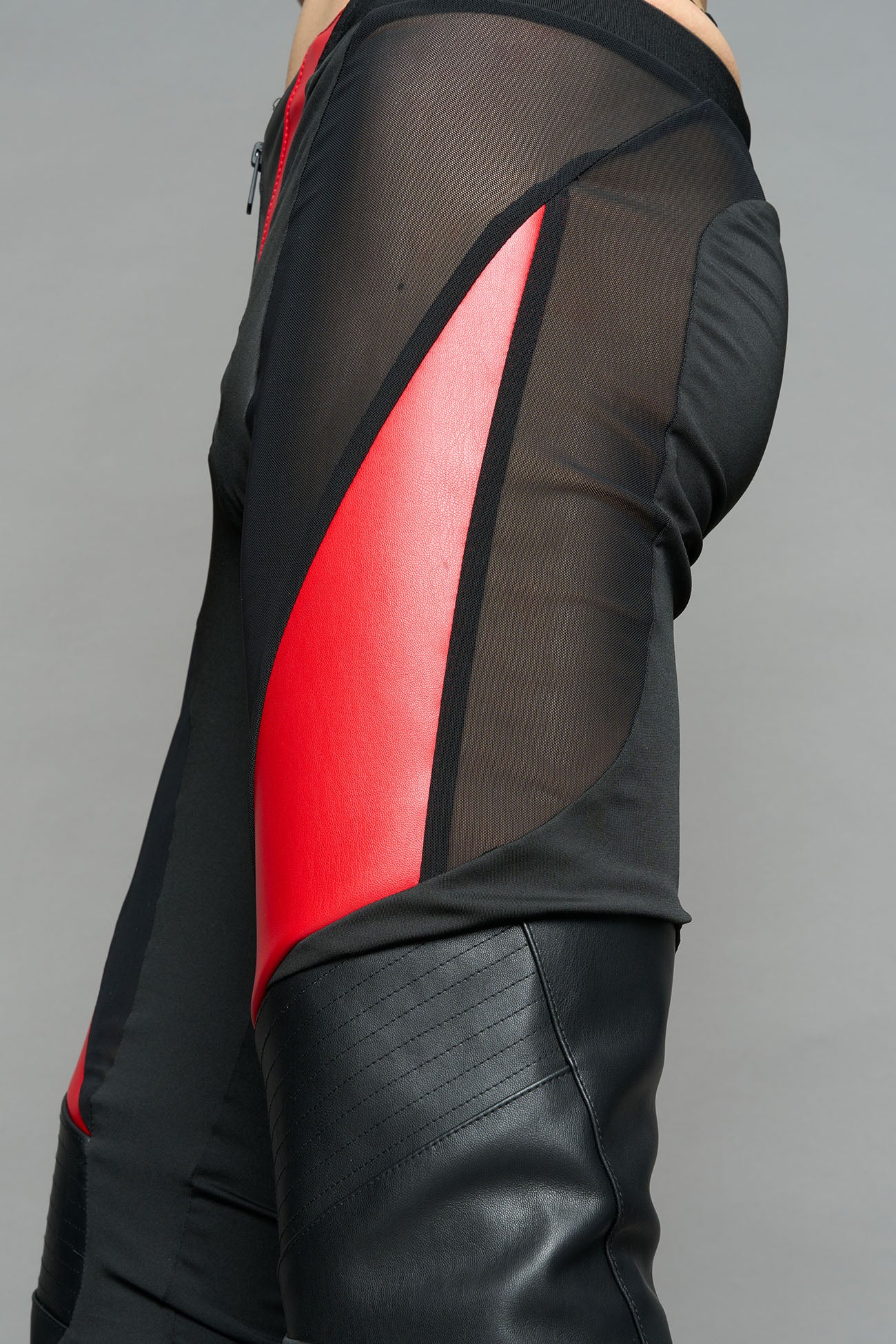Model wearing high-waisted black red vegan leather pants with mesh cutouts, moto-inspired paneling, and flared stacked legs – edgy streetwear trousers styled with chunky platform boots