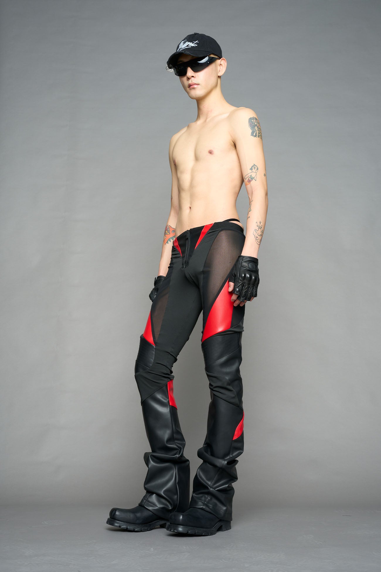 Model wearing high-waisted black red vegan leather pants with mesh cutouts, moto-inspired paneling, and flared stacked legs – edgy streetwear trousers styled with chunky platform boots