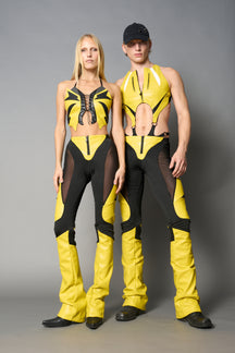 Model wearing high-waisted yellow vegan leather pants with mesh cutouts, moto-inspired paneling, and flared stacked legs – edgy streetwear trousers styled with chunky platform boots