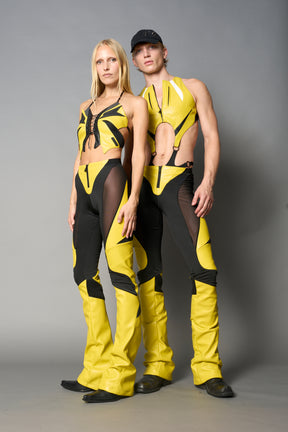 Model wearing high-waisted yellow vegan leather pants with mesh cutouts, moto-inspired paneling, and flared stacked legs – edgy streetwear trousers styled with chunky platform boots