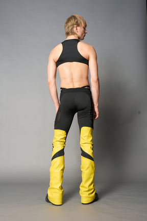 Model wearing high-waisted yellow vegan leather pants with mesh cutouts, moto-inspired paneling, and flared stacked legs – edgy streetwear trousers styled with chunky platform boots