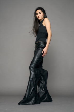 Black vegan leather stretch mutant pants with high waist, ribbed knee panels, and exaggerated flared legs by Namilia