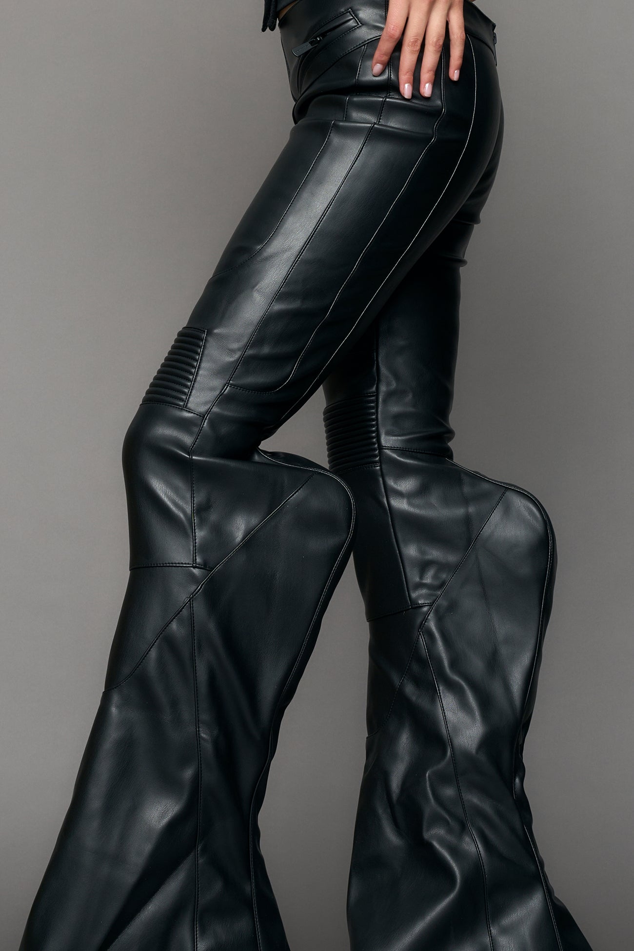 Black vegan leather stretch mutant pants with high waist, ribbed knee panels, and exaggerated flared legs by Namilia
