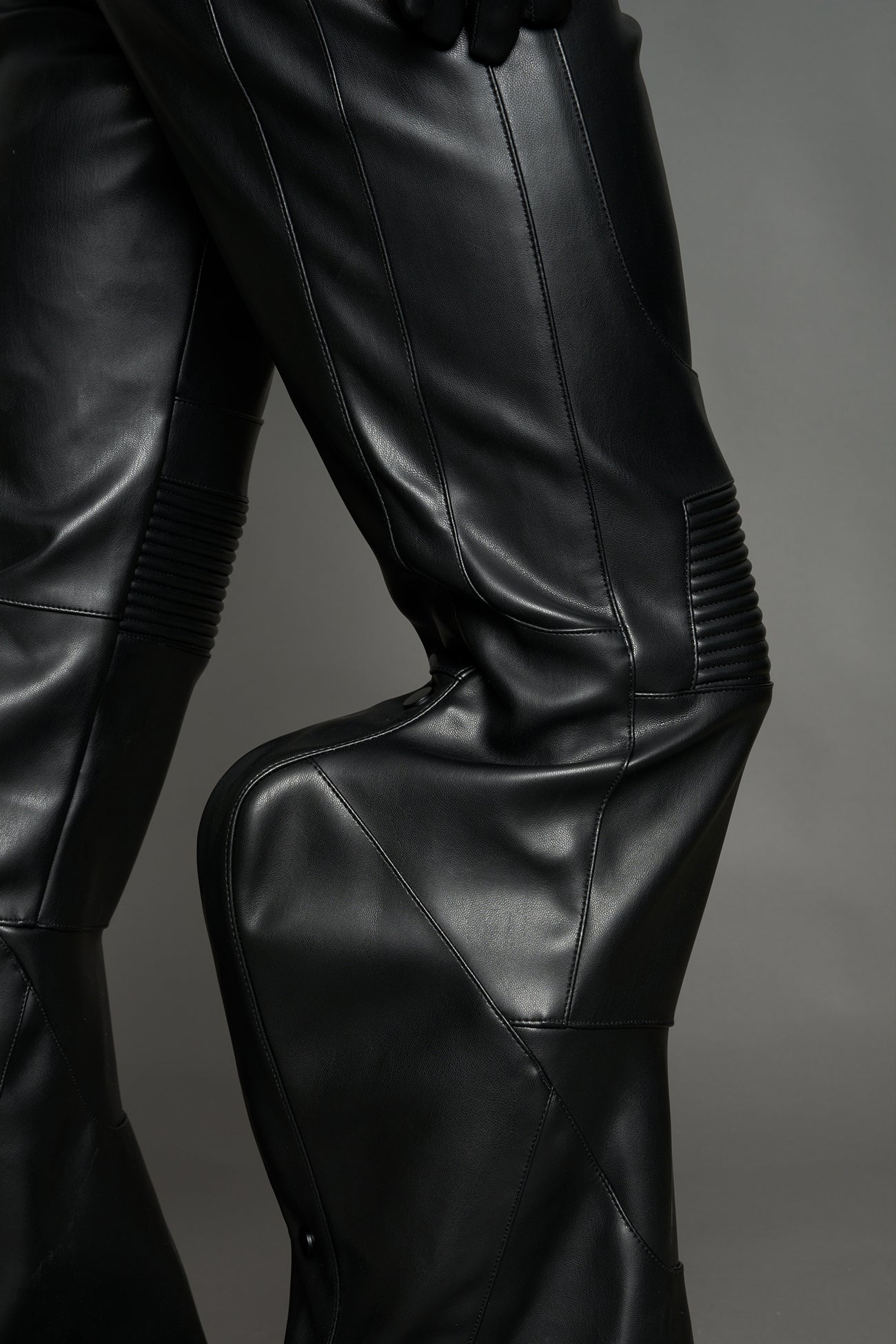 Black vegan leather stretch mutant pants with high waist, ribbed knee panels, and exaggerated flared legs by Namilia