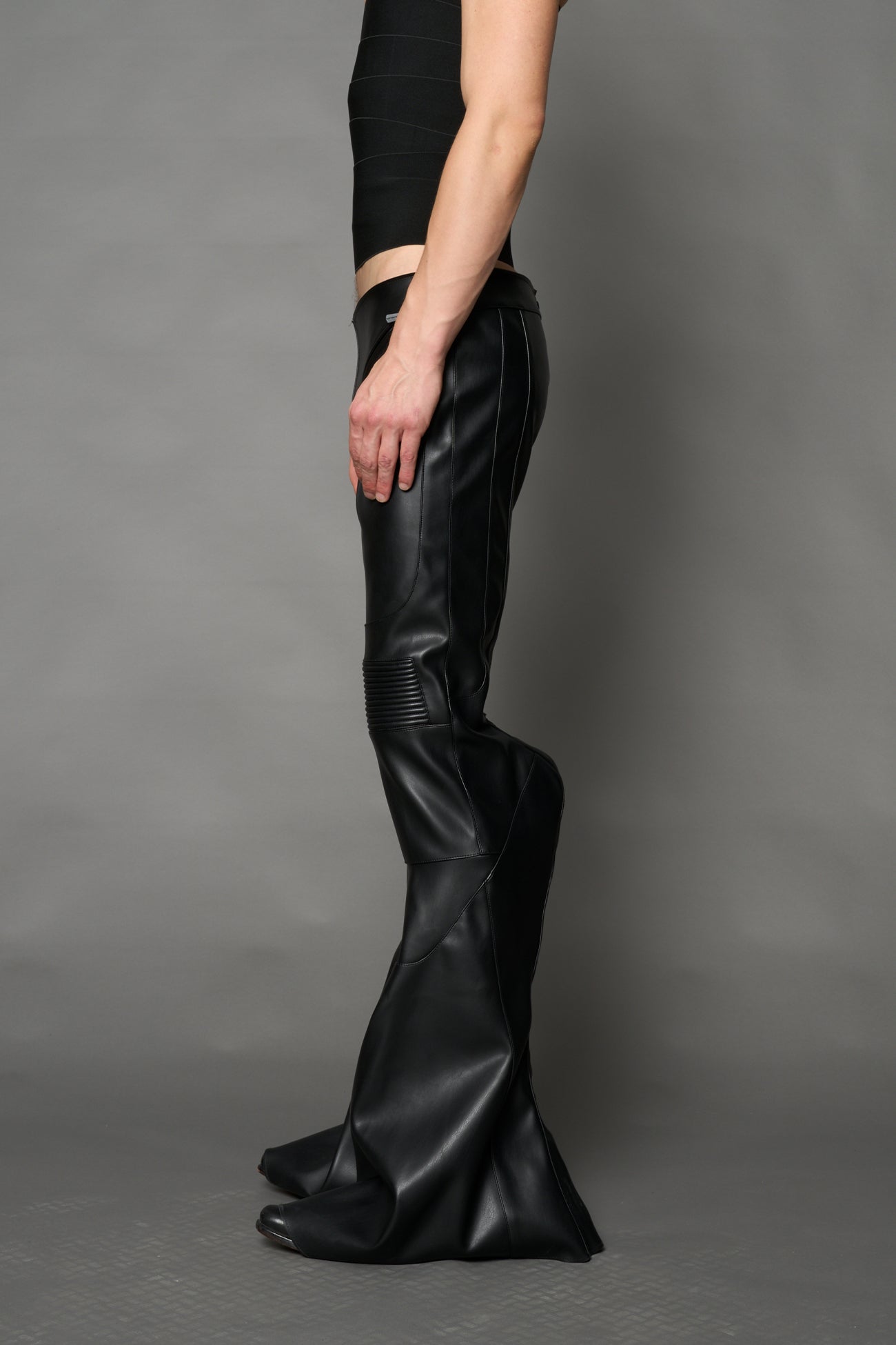 Black vegan leather stretch mutant pants with high waist, ribbed knee panels, and exaggerated flared legs by Namilia