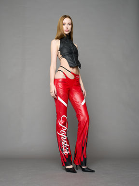 Model wears red vegan leather flare trousers with motocross paneling, padded details, flame and cross stitching, slogan embroidery, and an asymmetric waistband with adjustable elastic thong straps.