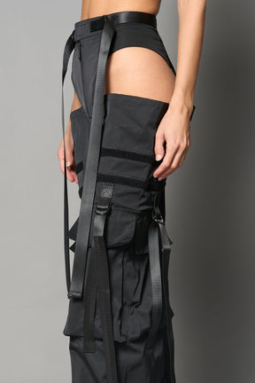 Black nylon cargo trousers with exposed high-cut panty waist, cut-out hips, oversized pockets, and adjustable utility straps – edgy streetwear and festival pants.