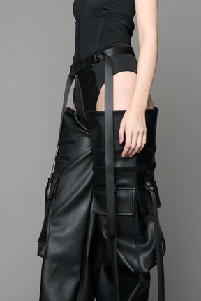Model wearing Black vegan leather panty trousers featuring an integrated stretch panel for comfort, adjustable belt detail, and a relaxed high-waist silhouette.