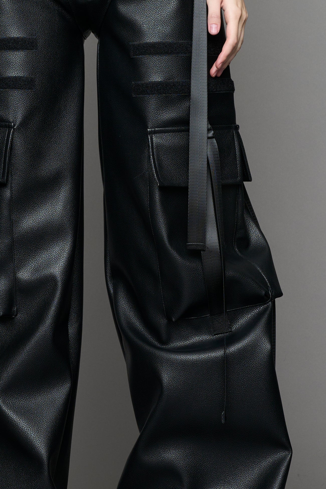 Model wearing Black vegan leather panty trousers featuring an integrated stretch panel for comfort, adjustable belt detail, and a relaxed high-waist silhouette.