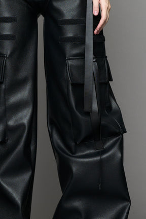 Model wearing Black vegan leather panty trousers featuring an integrated stretch panel for comfort, adjustable belt detail, and a relaxed high-waist silhouette.