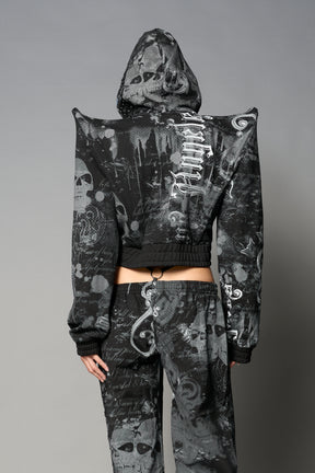 Model wearing a black print cropped hoodie with exaggerated spike shoulders, drawstring hood