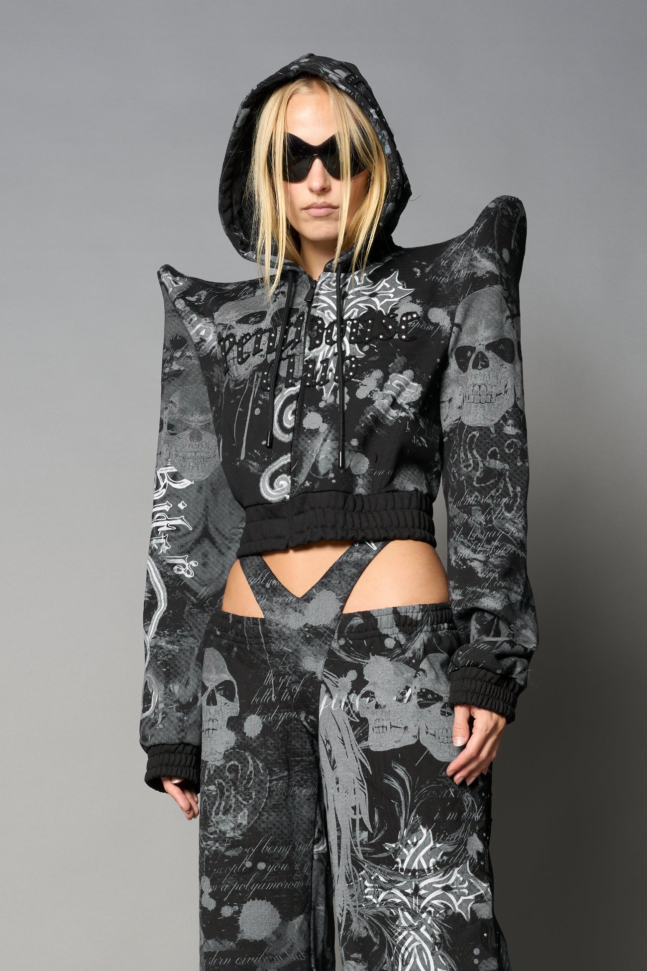 Model wearing a black print cropped hoodie with exaggerated spike shoulders, drawstring hood