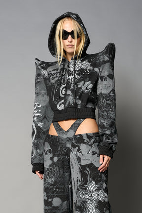 Model wearing a black print cropped hoodie with exaggerated spike shoulders, drawstring hood