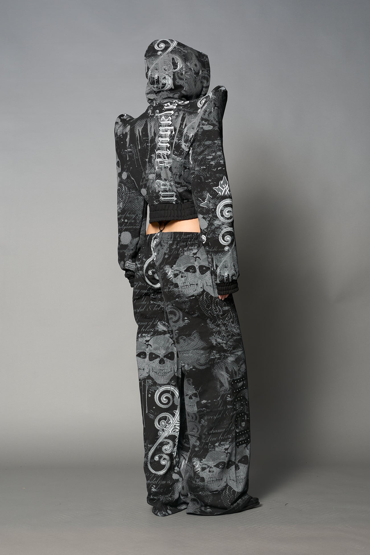 Model wearing a black print cropped hoodie with exaggerated spike shoulders, drawstring hood