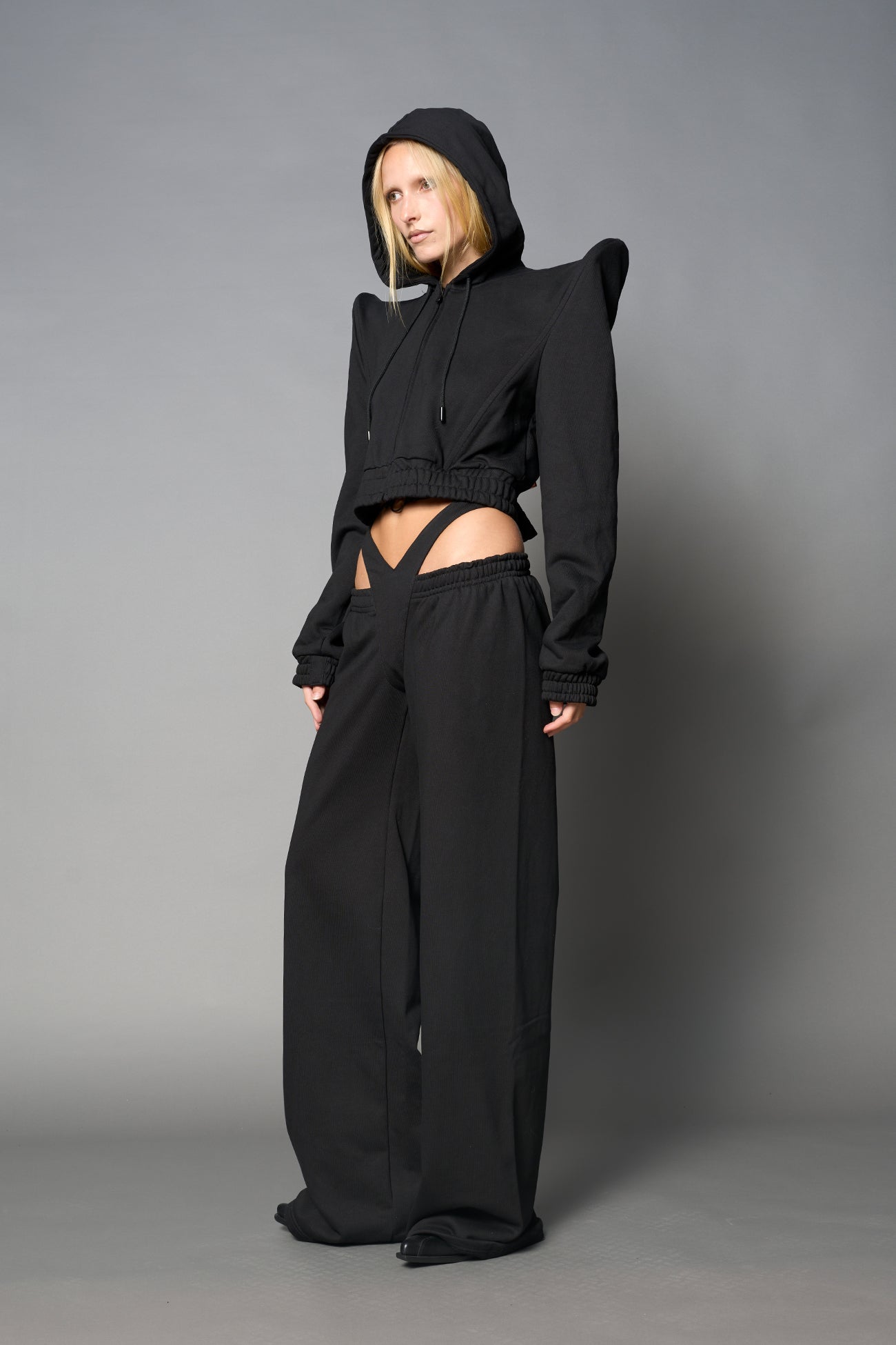 Model wearing a black cropped hoodie with exaggerated spike shoulders, drawstring hood