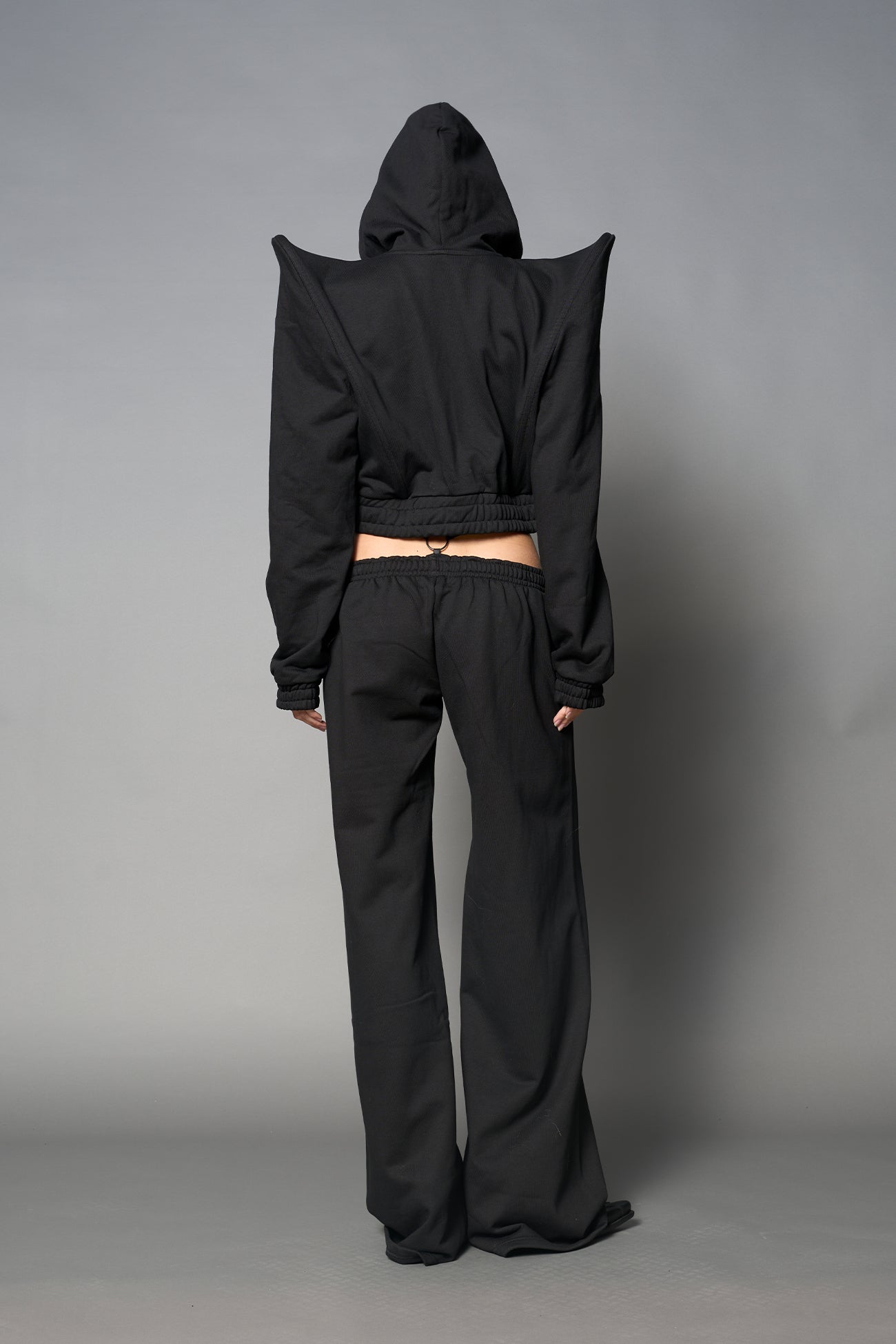 Model wearing a black cropped hoodie with exaggerated spike shoulders, drawstring hood