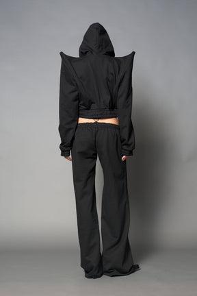 Model wearing a black cropped hoodie with exaggerated spike shoulders, drawstring hood