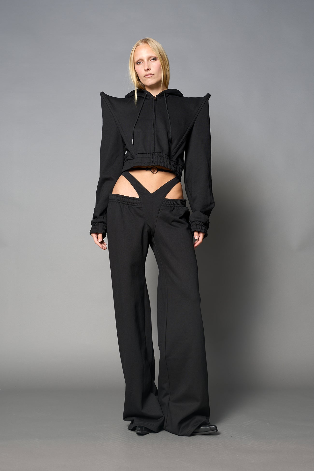 Model wearing a black cropped hoodie with exaggerated spike shoulders, drawstring hood