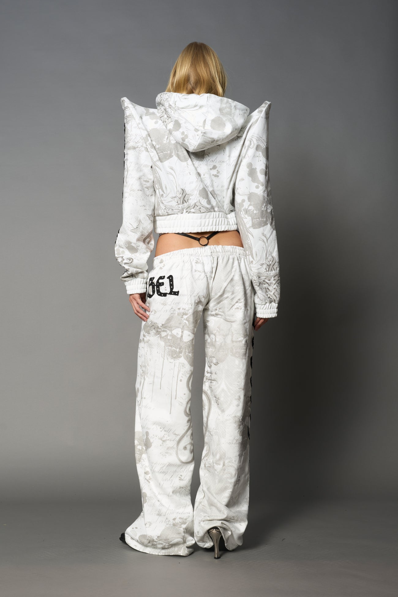 Model wearing a white print cropped hoodie with exaggerated spike shoulders, drawstring hood