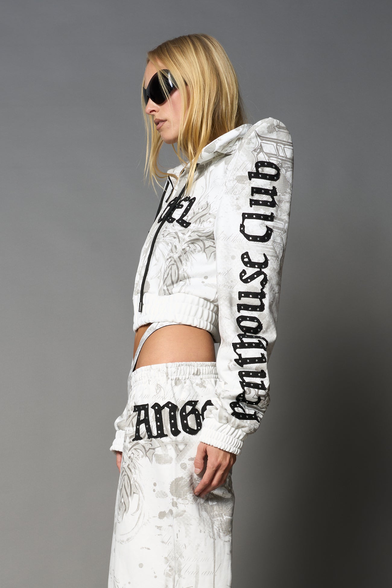 Model wearing a white print cropped hoodie with exaggerated spike shoulders, drawstring hood